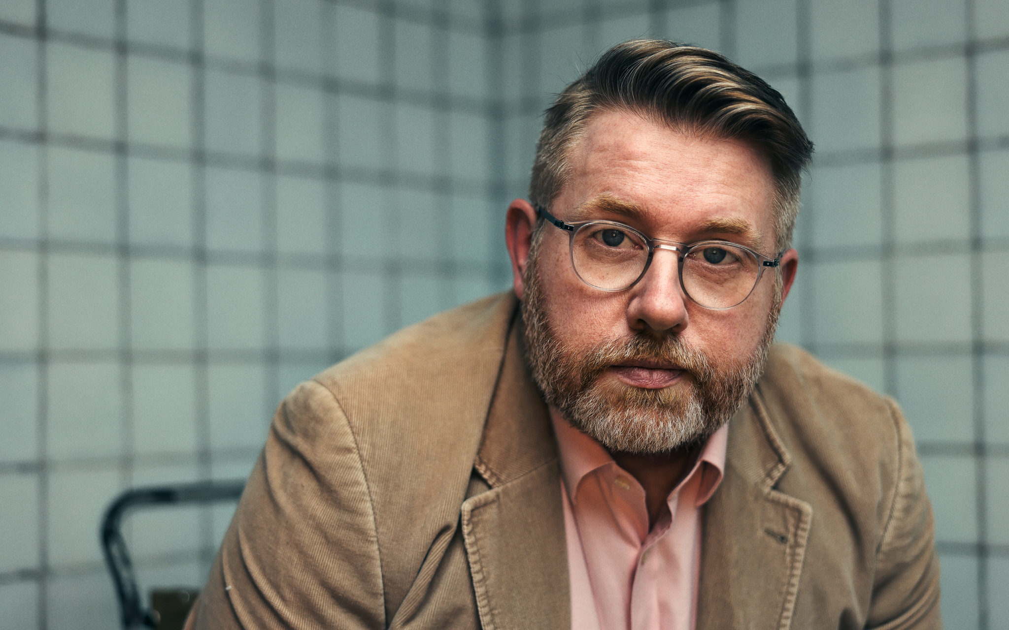 Trev is a red haired man with glasses and a red beard. He wears a black t-shirt against a grey backround